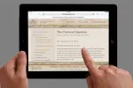 Hands holding a tablet, finger touching the screen with text displayed.