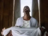 Man in white robe screams in anguish, holding a lifeless body wrapped in cloth.